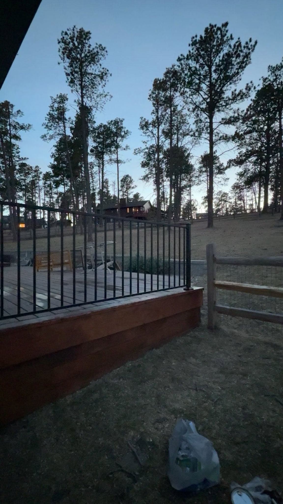 A stained deck with a black iron rail, looking out over open ground and pines