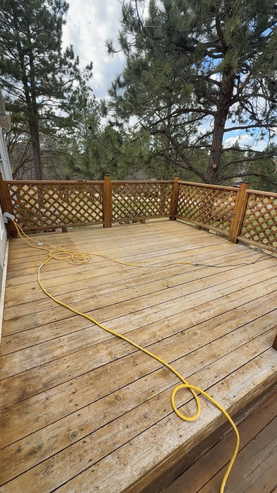A deck part way through: boards washed back to pale timber with the hose still run across them