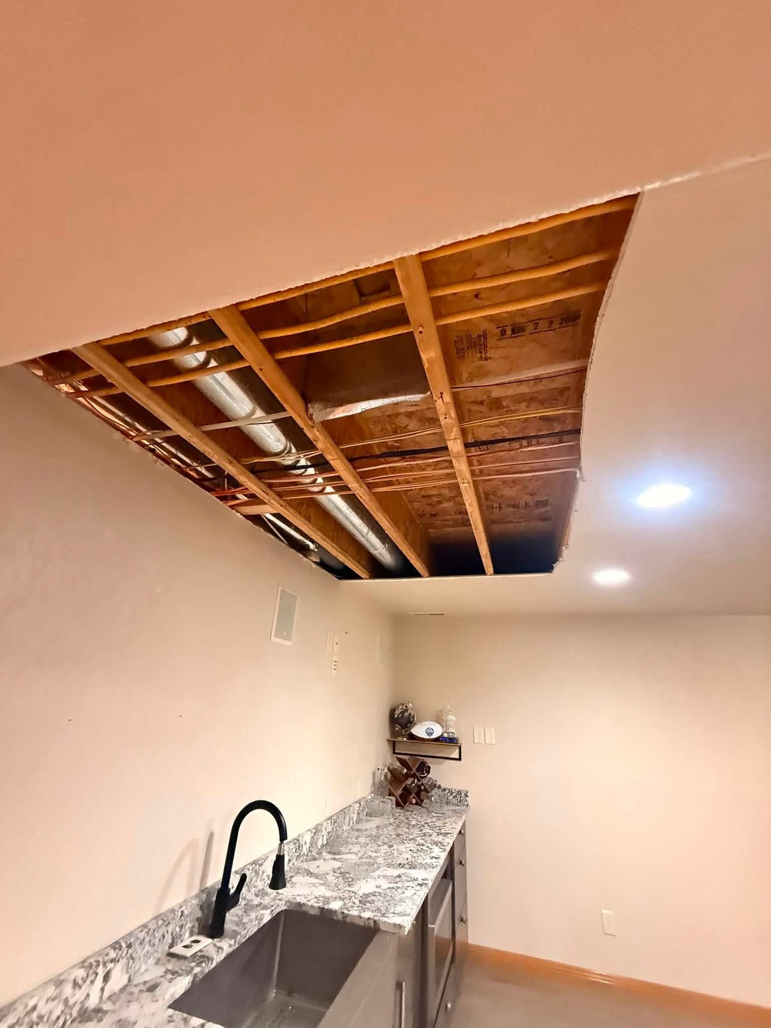 A ceiling opened to the joists over a kitchenette counter, the granite top and sink below still in place