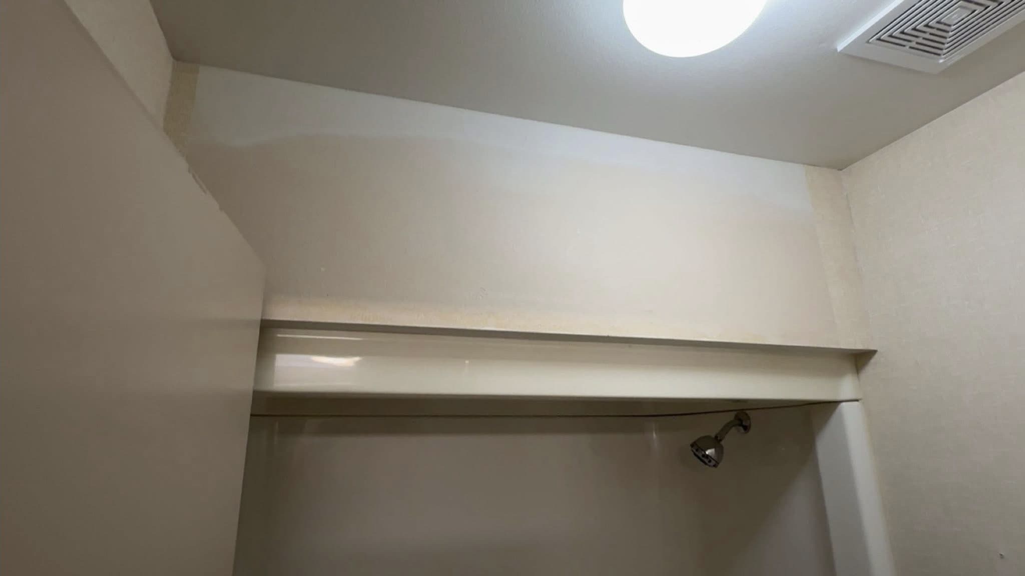 The head of a shower alcove after patching and painting: a shelf across the end wall, an extract vent and a ceiling light above, the showerhead below