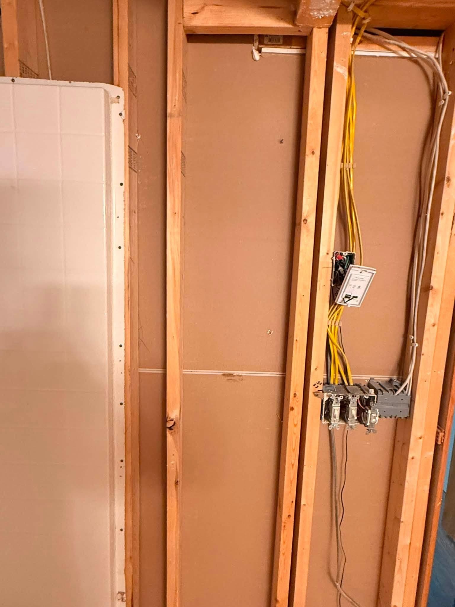 A single stud bay opened up, cabling gathered into a junction box, with the edge of a new board set against it