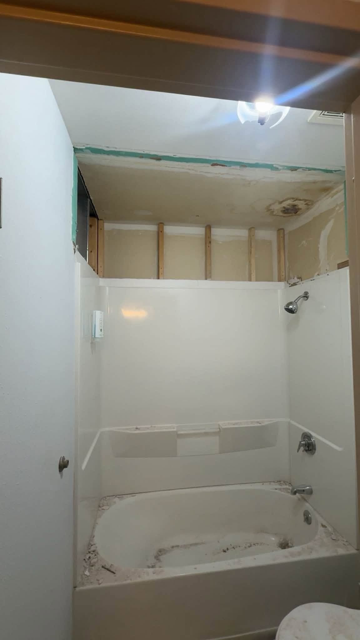 A tub and shower alcove with the wall above it opened up, the surround still in place below