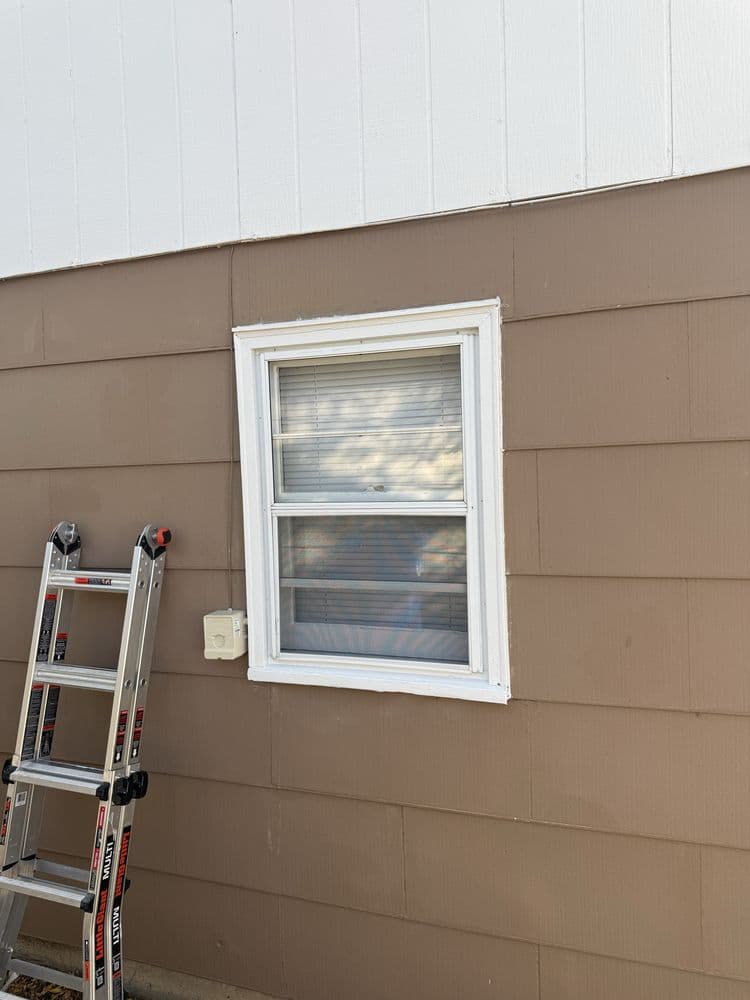 Two-tone exterior — white upper gable over tan lap siding — with a ladder set against the wall beside a white-trimmed window