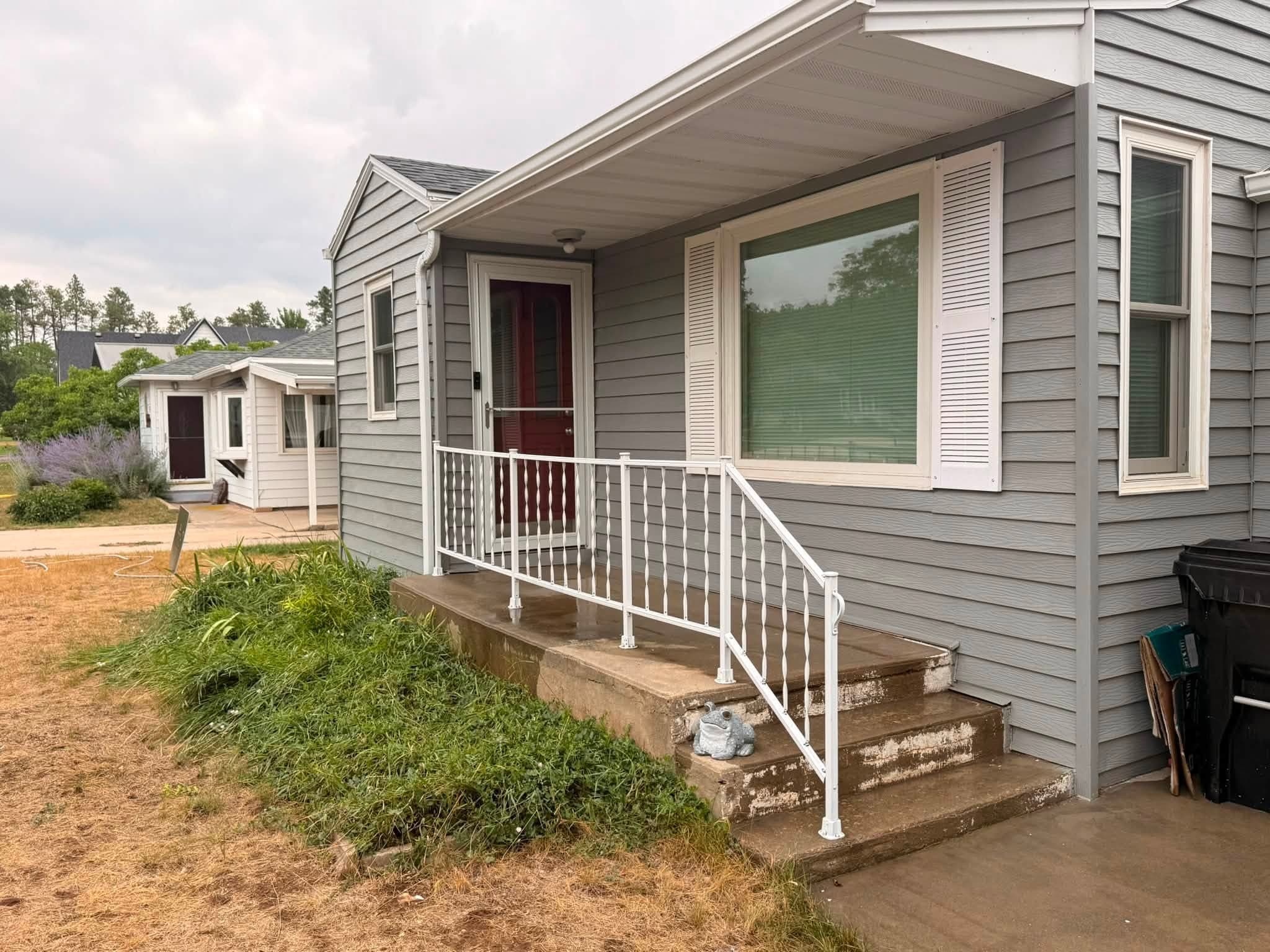 The same house finished: gray lap siding with white trim and soffit, a white porch railing and a red entry door