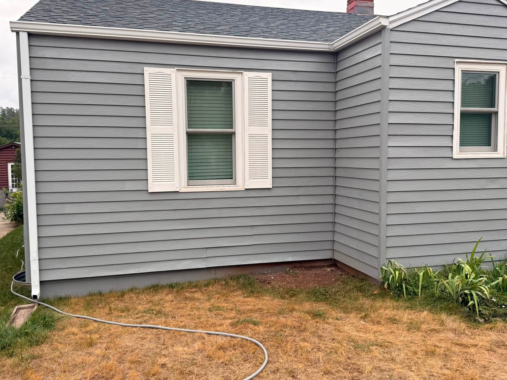 Finished corner elevation in gray with white window trim and shutters, showing the returned wall and the fascia line