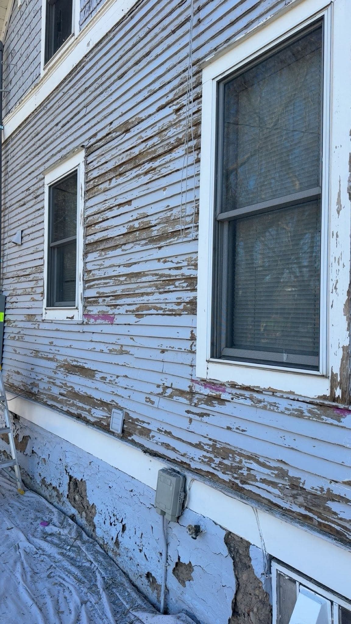 Heavy coating failure below a window: paint curling away from the boards in long strips down to bare wood