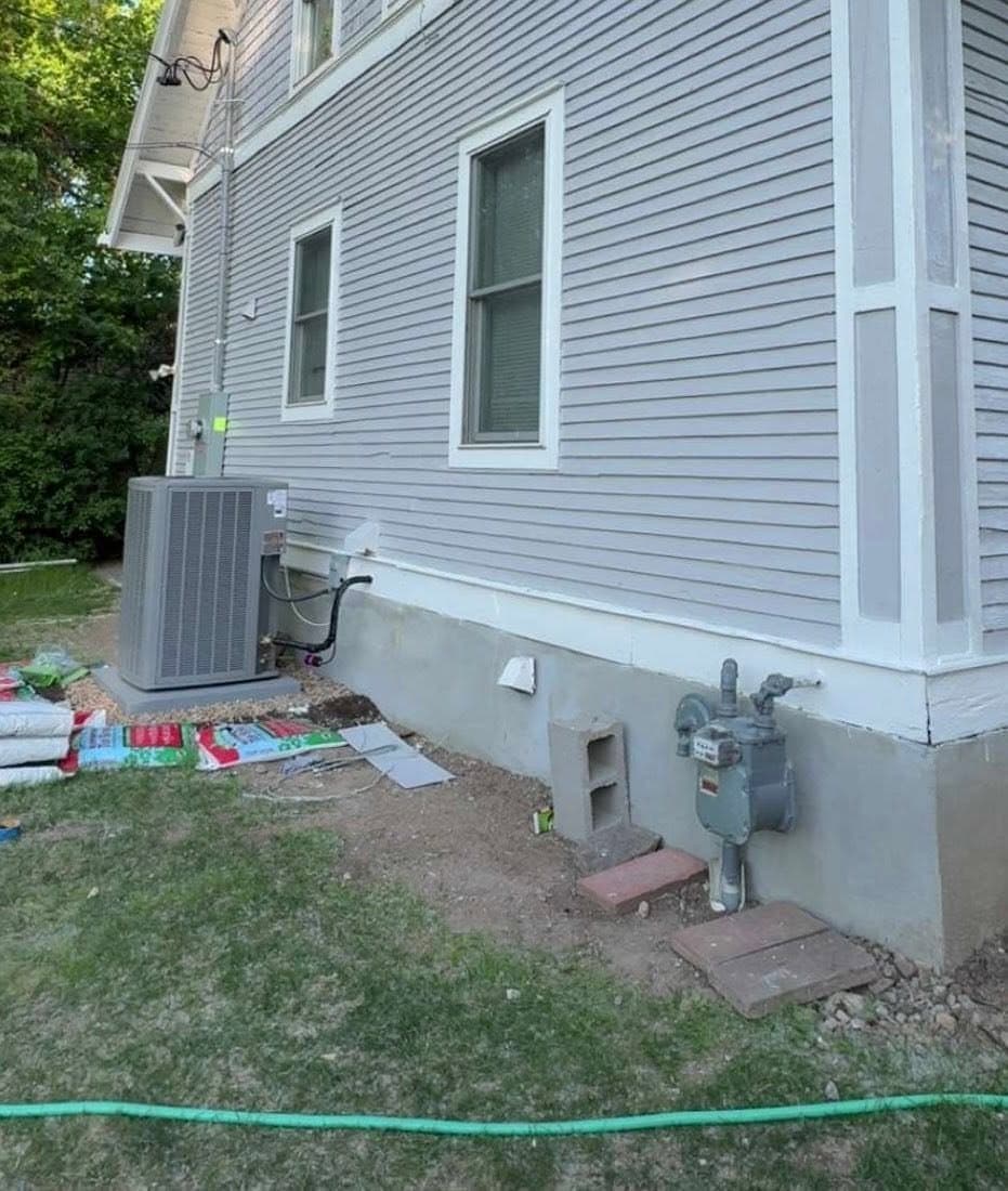 A finished two-story elevation in pale blue-gray with white trim, an air-conditioning unit and meter set at the base