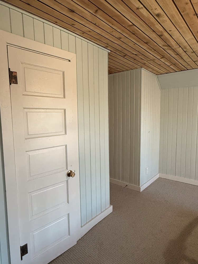 Corner of the same cedar-ceilinged room, showing freshly painted white paneling, door and trim