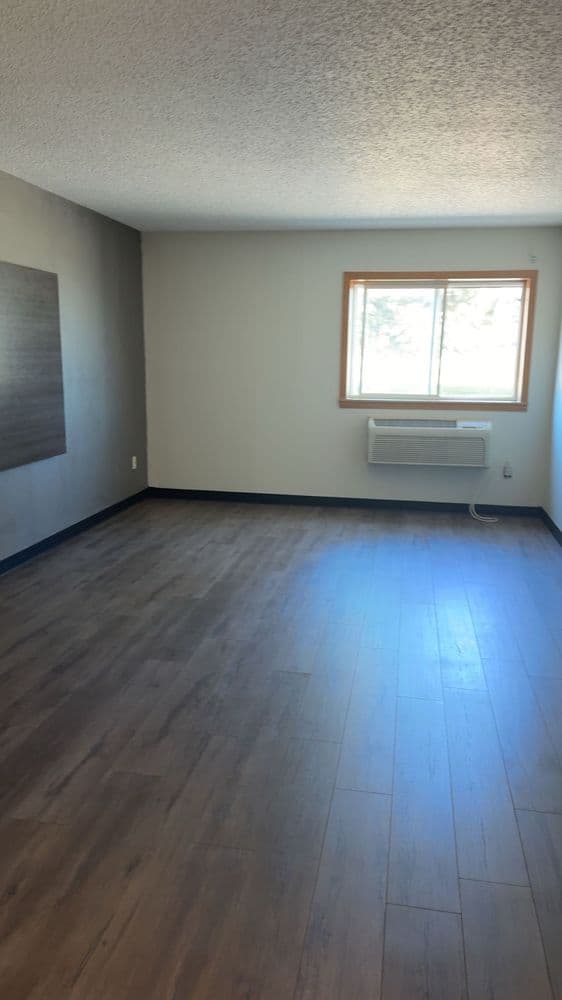 Empty finished room with freshly painted walls, a textured ceiling and a window above a through-wall air unit