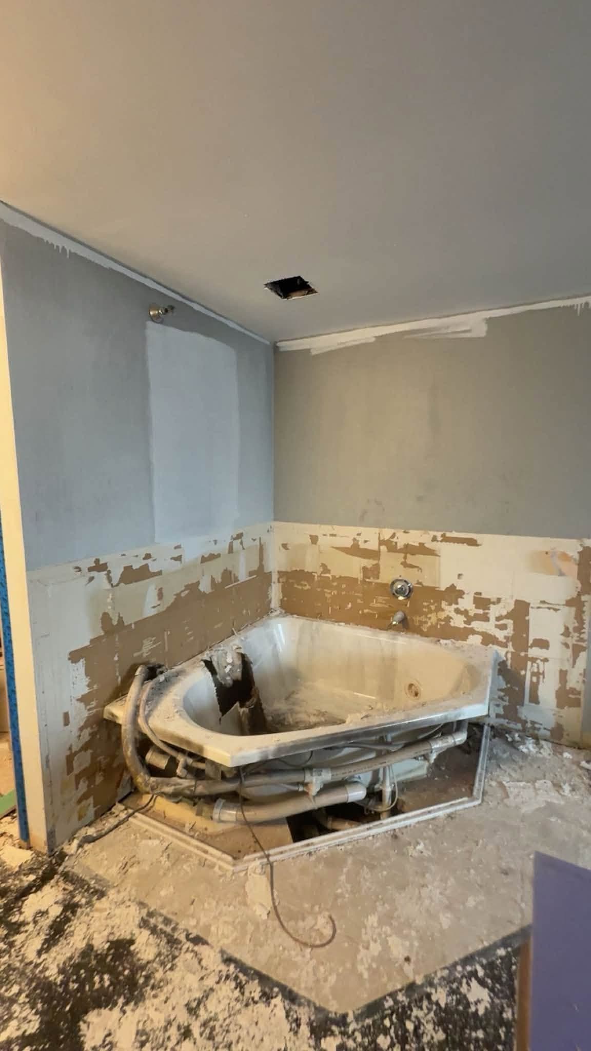 A corner tub with the surround torn back to the framing and the floor stripped, mid-demolition