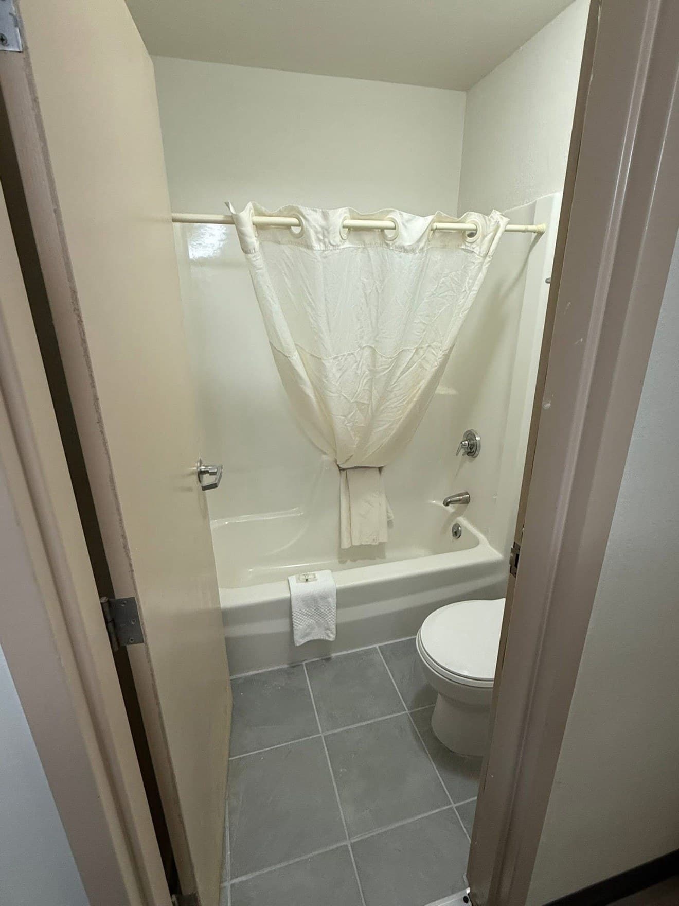 A finished bathroom seen through the doorway, with a tub and shower curtain, a WC and gray tile flooring