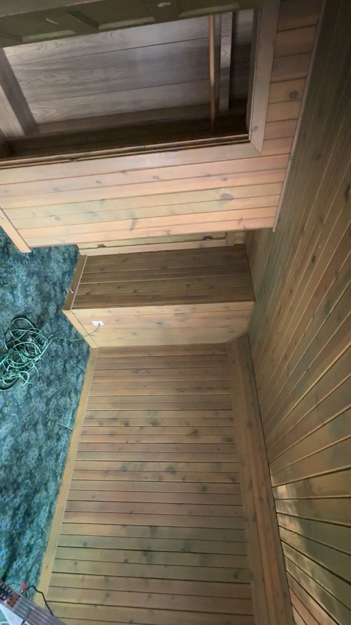 A stair and landing lined in cedar boards, looking down to a green-tiled floor below