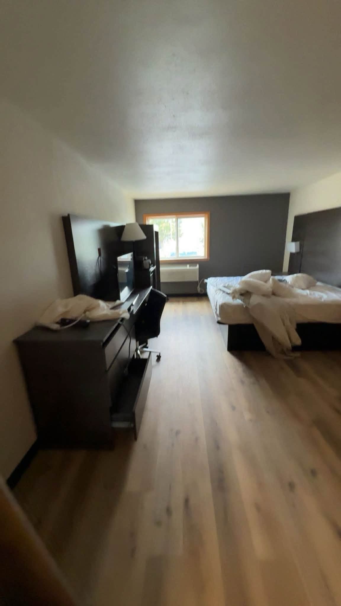 A finished room with plank flooring, seating in the foreground and a bed made up by the window