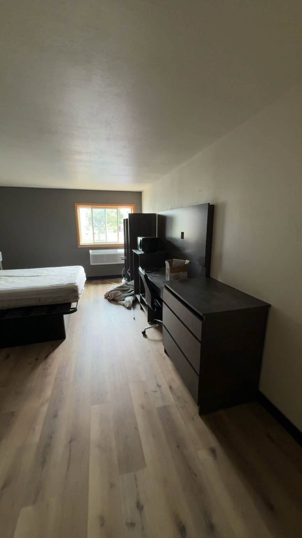 A finished guest room with plank flooring, a dresser and television, and a bed made up under the window
