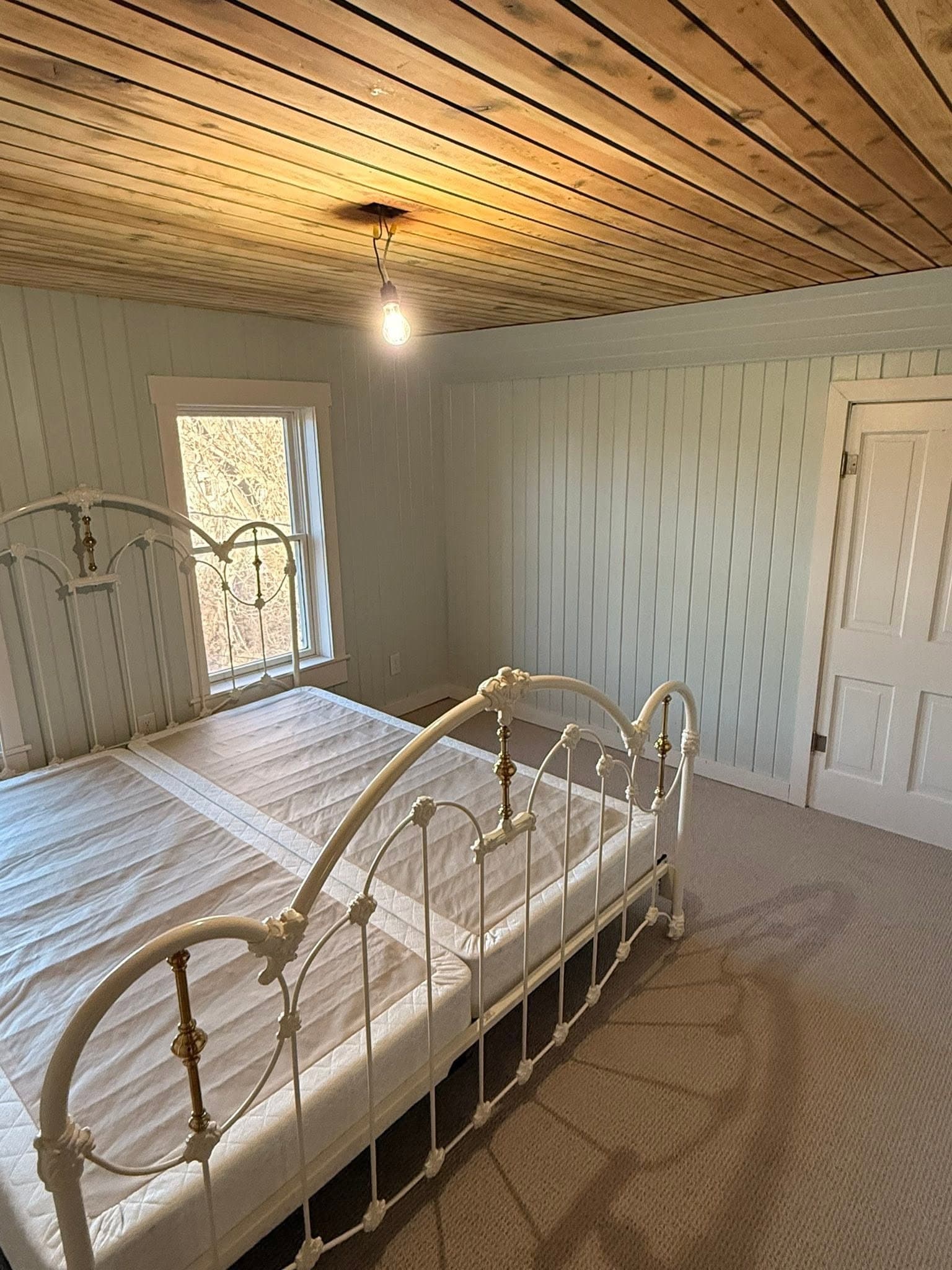 A paneled bedroom with a timber plank ceiling and a pendant light, a metal bed frame against the wall