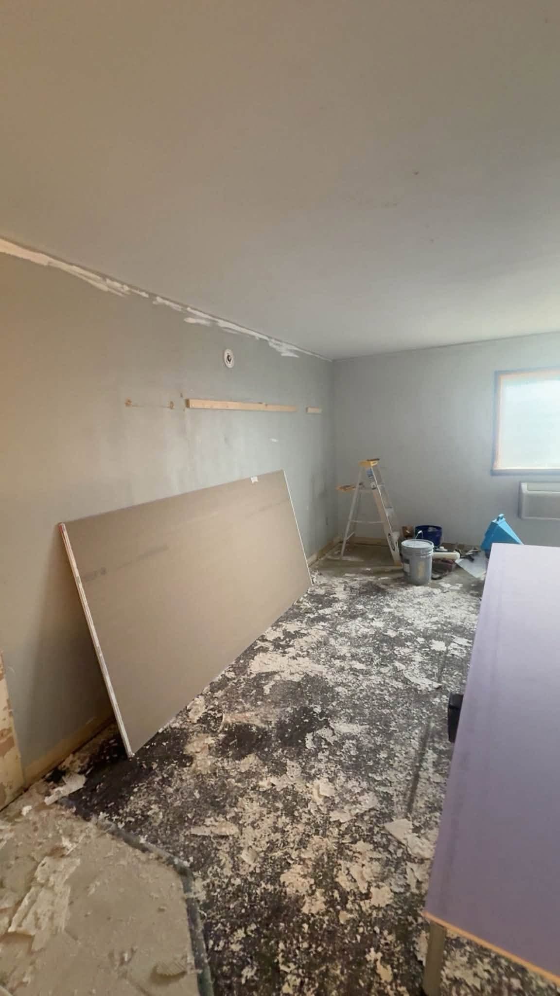 A room stripped back, a sheet of board leaning against the wall and the floor covered in torn-up material