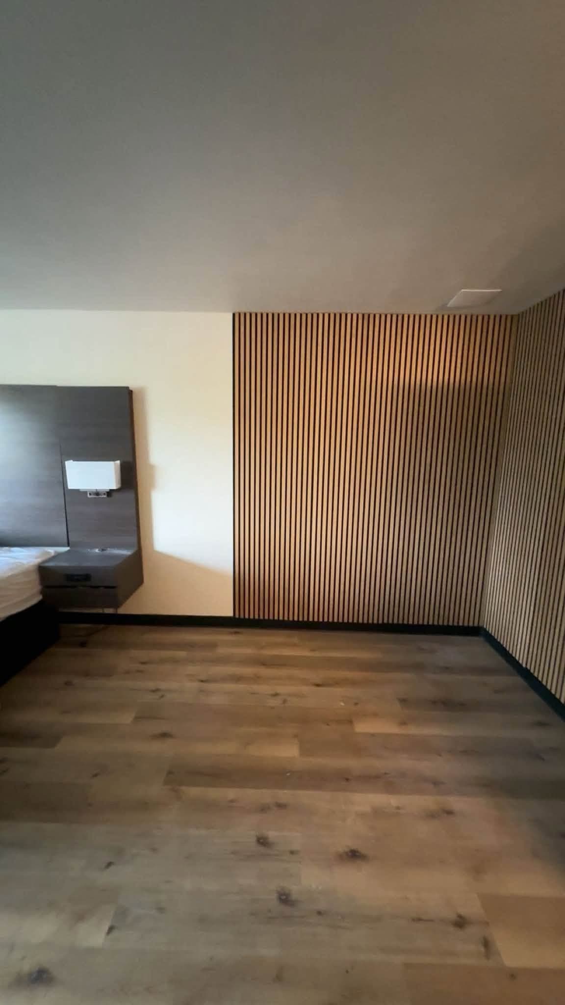 A room finished with a slatted timber accent wall running floor to ceiling, against wide plank flooring