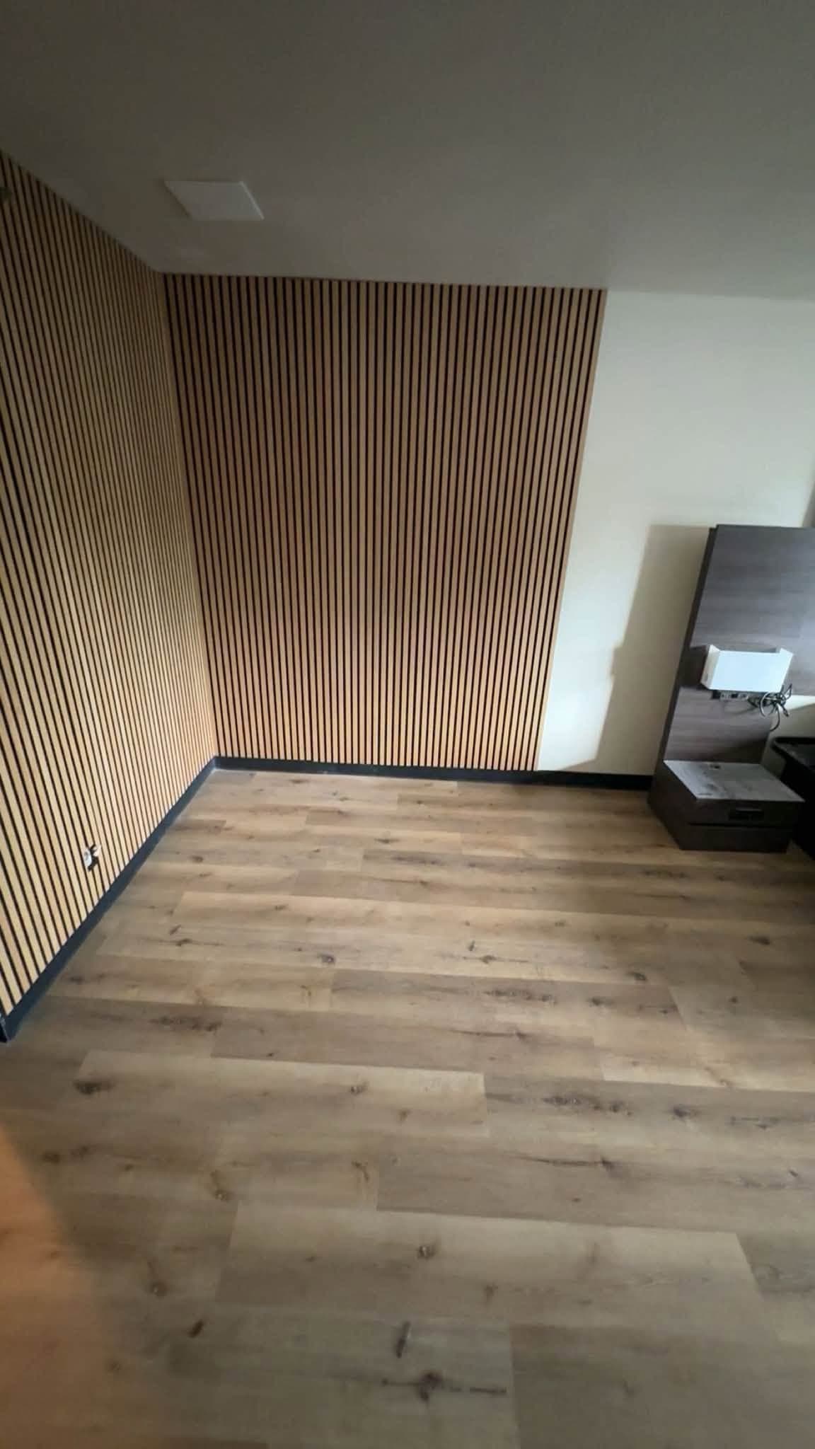 A slatted timber wall meeting plain painted walls, with wide plank flooring laid up to it