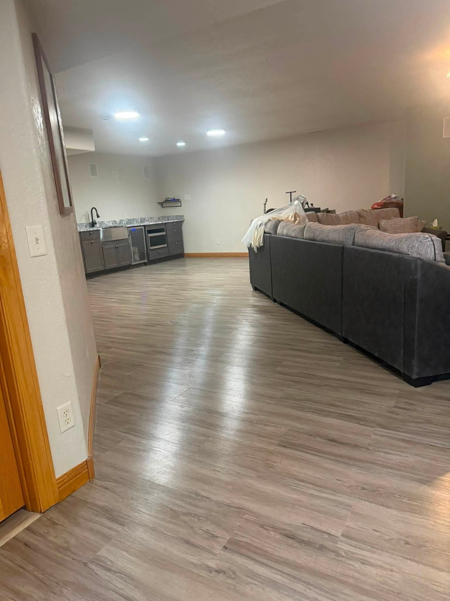 An open suite finished out, with plank flooring laid, a kitchenette along one wall and seating and a bed at the far end