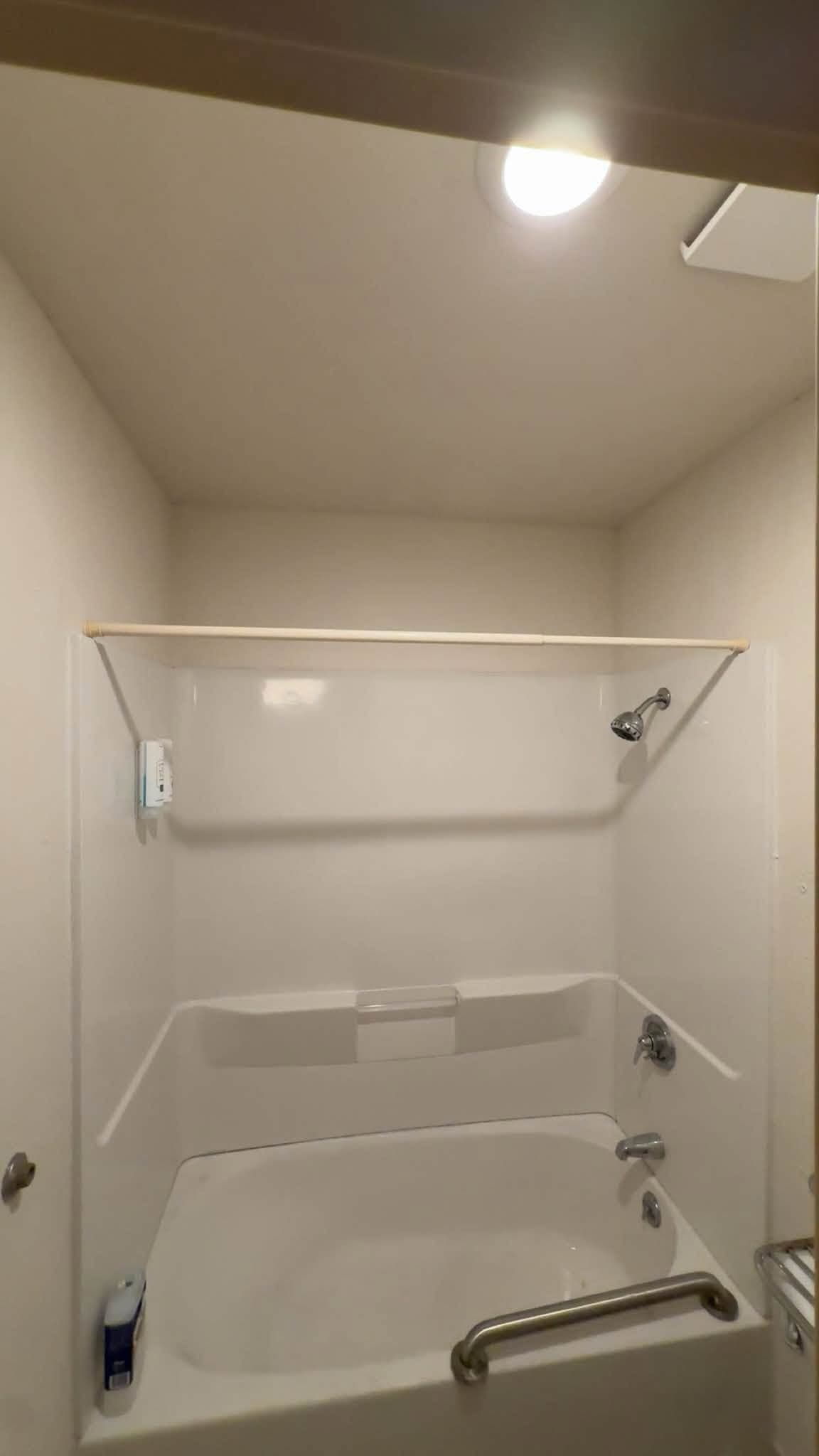 A finished tub and shower alcove in white, with a grab rail and a shelf across the end wall