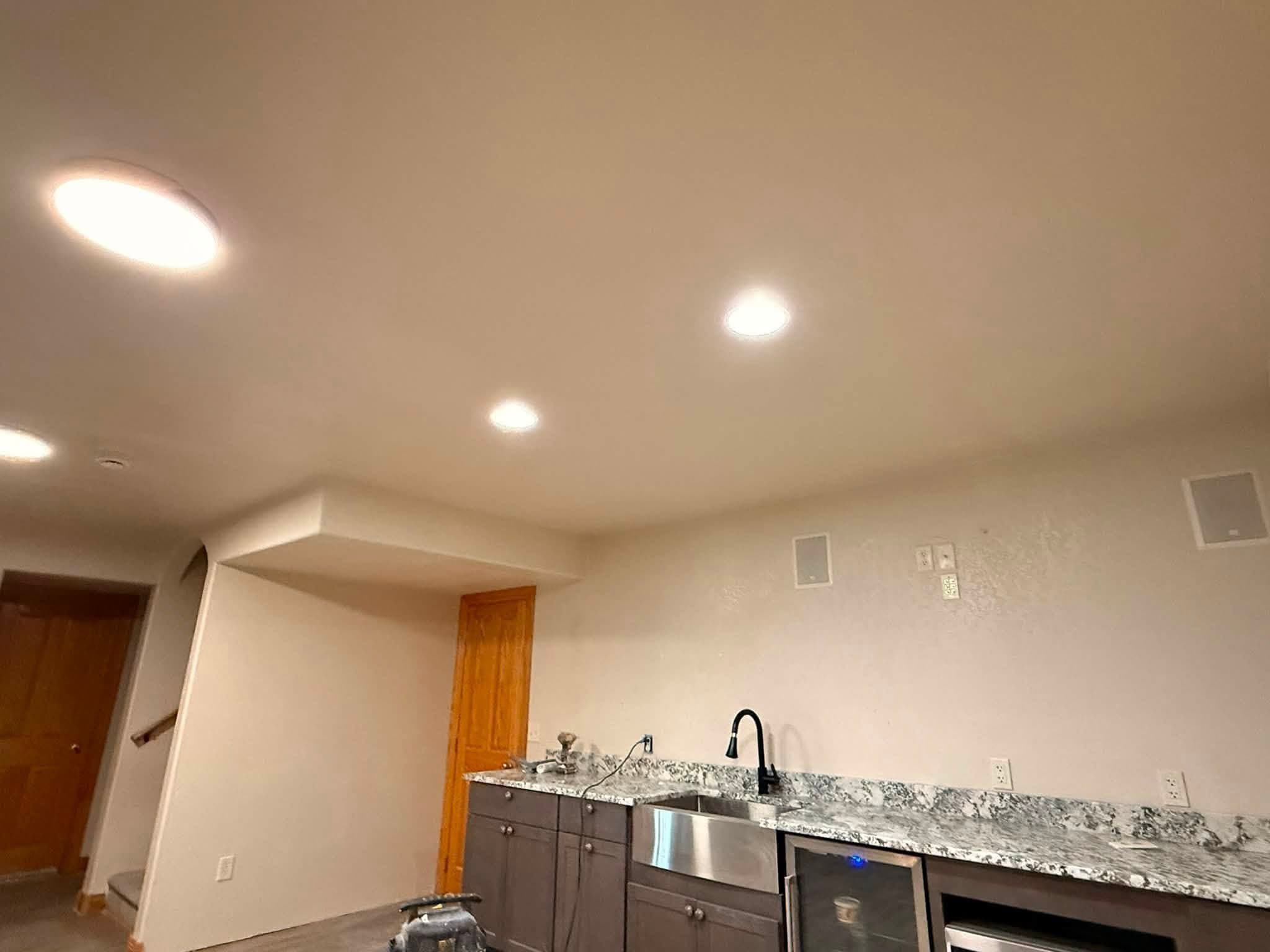 A finished wet bar with a granite counter, dark cabinetry, an undercounter fridge and recessed lighting