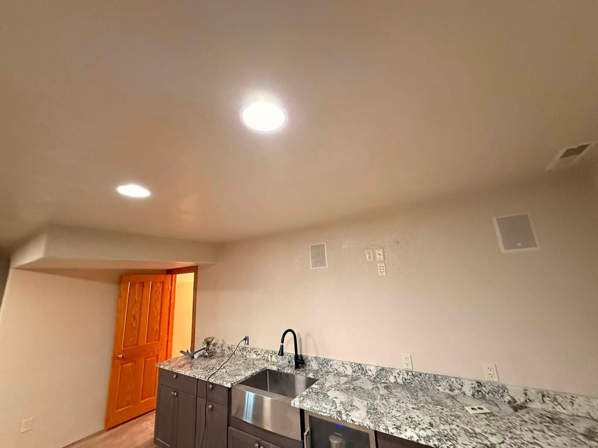 A wet bar run finished end to end: granite counter, undermounted sink and dark cabinets, with a timber door beyond