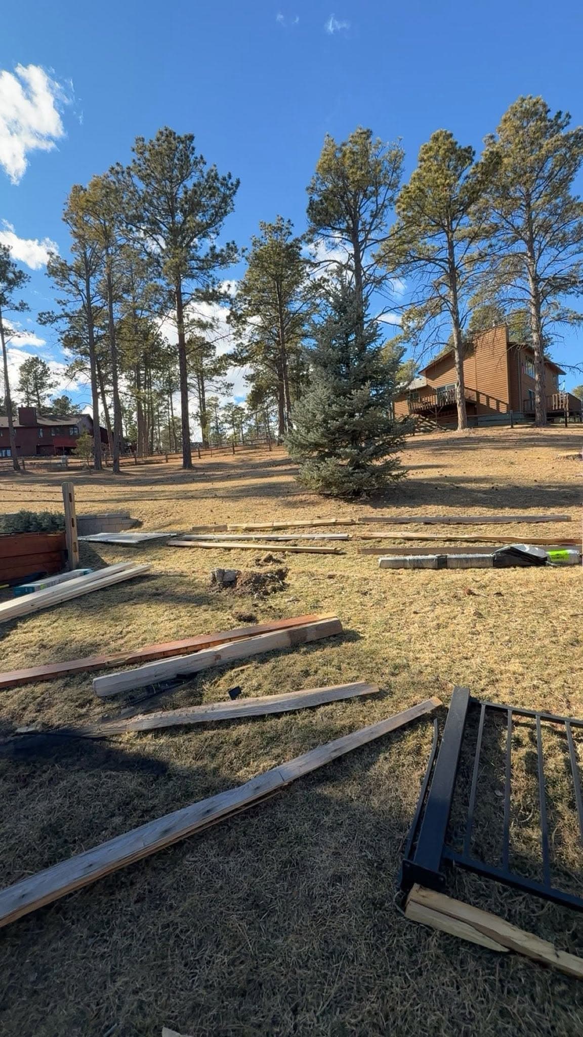 Fence rails and posts lying on the grass where they came down, with the treeline behind